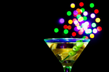 A martini glass with green olives on a black background