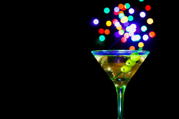 A martini glass with green olives on a black background