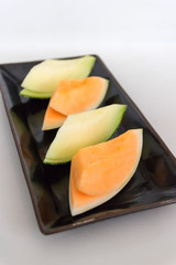 Juicy melon sliced on black porcelain tray.