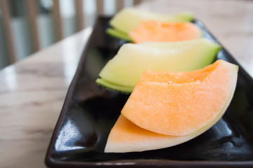 Juicy melon sliced on black porcelain tray.
