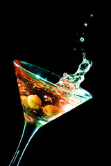 A martini glass with green olives on a black background