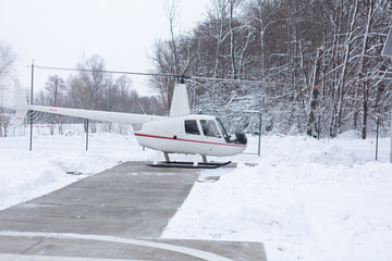 White helicopter with red line landed on the ground in winter and snow on the ground