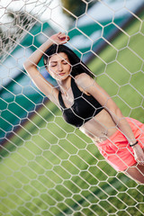 Front view of sexy woman hold ball in hand after penalty kick. Goalkeeper stand in gate behind stadium with seat on background. Female sport idea