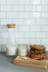 Stack of Homemade Salted Chocolate Chip Cookies with glass of milk, White Subway Tile Background, Wooden Plate