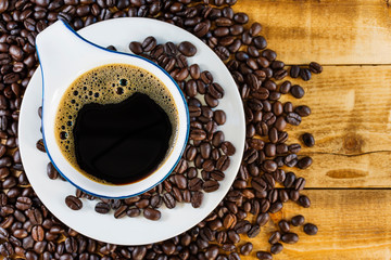 Black coffee in a white coffee cup And roasted coffee beans placed on the old wooden floor, top view