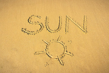 Fototapeta na wymiar Top view of the word Sun hand written in the sand with a drawing representing it. Summer and weather concept..