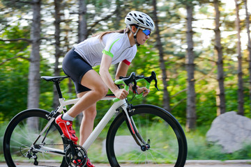 Young Woman Cyclist Riding Road Bicycle on the Free Road in the Forest at Hot Summer Day. Healthy Lifestyle Concept.