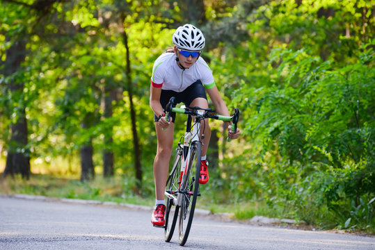 Young Woman Cyclist Riding Road Bicycle on the Free Road in the Forest at Hot Summer Day. Healthy Lifestyle Concept.