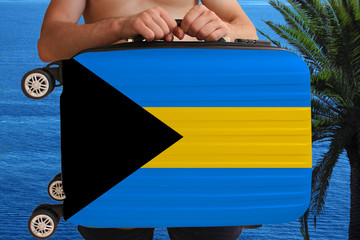 tourist holds with two hands a suitcase with the national flag of Bahamas, a symbol of vacation, immigration,