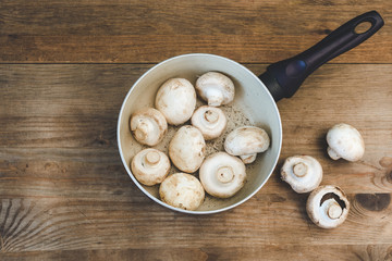 Bowl of fresh champignon mushrooms on wooden background