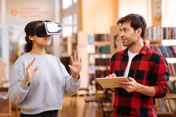 Young man with tablet interacting with his classmate in vr headset