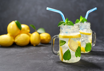 Refreshing chilled lemonade in jars on a black background  with fresh lemon.