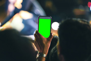 Hands of people holding mobile smart phone with green screen recording and taking a picture at...