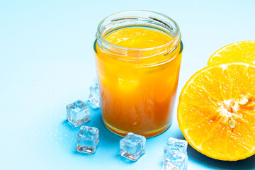 Glass of orange juice with sliced orange fruit and ice cubes on blue background