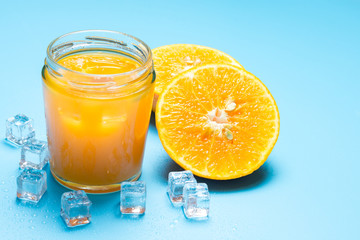 Glass of orange juice with sliced orange fruit and ice cubes on blue background