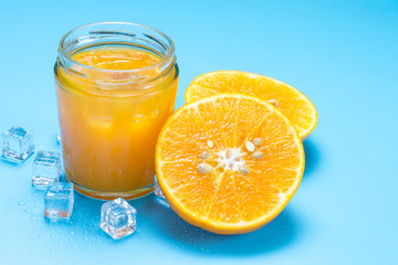 Glass of orange juice with sliced orange fruit and ice cubes on blue background