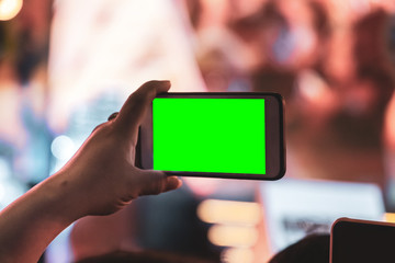 Hands of people holding mobile smart phone with green screen recording and taking a picture at music concert