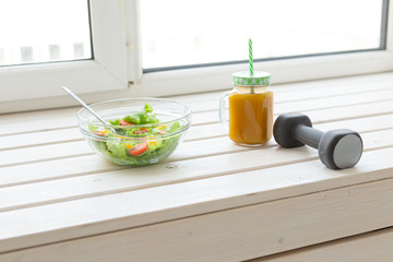 Vegetable salad and fruit smoothies and dumbbell lie on a white windowsill. Concept of healthy lifestyle physical activity and proper nutrition.