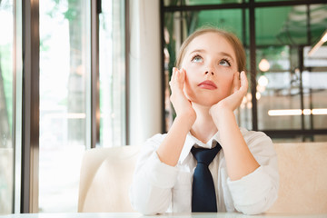 Girl meditates over cup of tea. Business child in tie and shirt