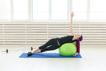 Young slim girl does exercise and stretching on a green fitball In the bright gym. Healthy back and ligament concept.