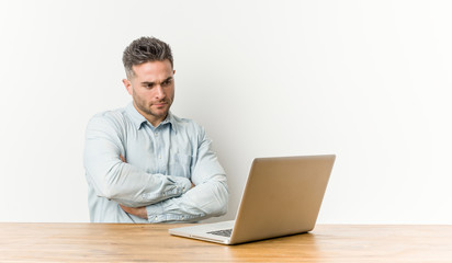 Young handsome man working with his laptop who feels confident, crossing arms with determination.