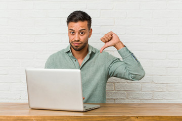 Young filipino man sitting working with his laptop showing a dislike gesture, thumbs down....