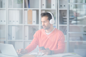 Obraz na płótnie Canvas Casual young businessman in headphones using modern gadgets