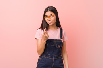 Young pretty arab woman wearing a jeans dungaree pointing with finger at you as if inviting come closer.