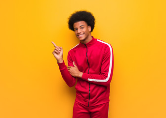 Young sport black man over an orange wall pointing to the side with finger