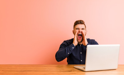 Young man working with his laptop shouting excited to front.