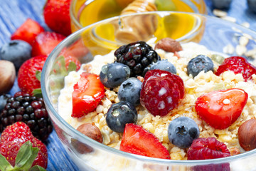 healthy muesli with raspberry, blueberry, strawberry, BlackBerry, hazelnut, milk and honey on blue wooden rustic table. homemade muesli or granola with honey, milk, fresh berries and nuts
