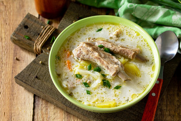 Vegetable soup with cabbage, sour cream and meat ribs on a kitchen wooden table.