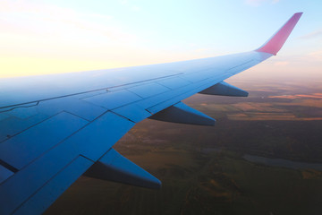 View from the porthole - Wing of an airplane taking off above the runway at high speed during the sunset. The land is running under the wing