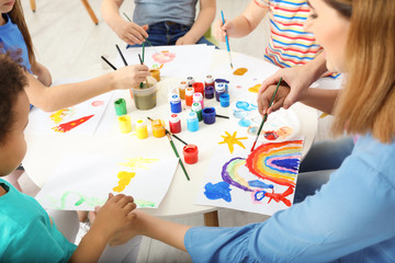 Female teacher with children at painting lesson indoors