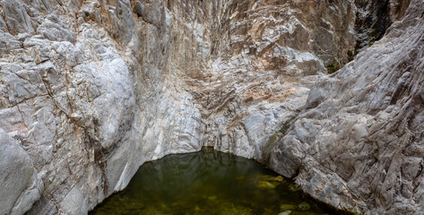 A hidden waterhole with clam water in a canyon with grey rock cliffs.
