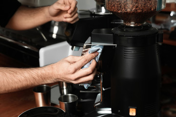 Barista cleaning coffee grinding machine with rag in cafe, closeup