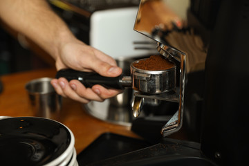 Fototapeta na wymiar Barista pouring milled coffee from grinding machine into portafilter, closeup