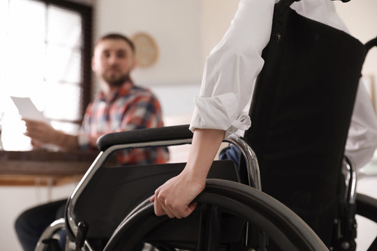 Woman in wheelchair with her colleague at workplace, closeup