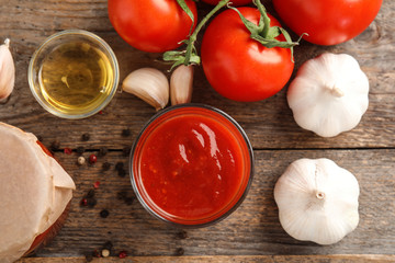 Flat lay composition with glass of tomato sauce, oil and vegetables on wooden table