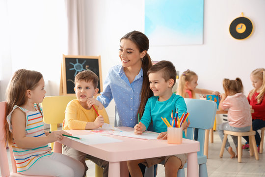 Little children with kindergarten teacher drawing at table indoors. Learning and playing