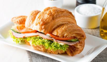 Fresh croissant or sandwich with salad, ham, jamon, prosciutto, salami, cheese, chicken, tomatoes on wooden background. Morning breakfast concept. Healthy and fast food.
