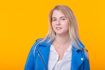 Nice young positive girl blonde in blue leather jacket posing on a yellow background. Happy young woman concept.