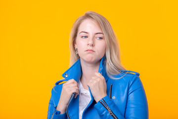 Young sad girl blonde in blue leather jacket posing on a yellow background. Melancholy young woman concept.