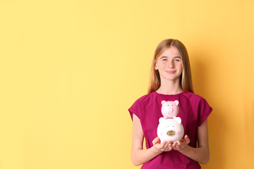 Fototapeta na wymiar Teen girl with piggy banks on color background. Space for text