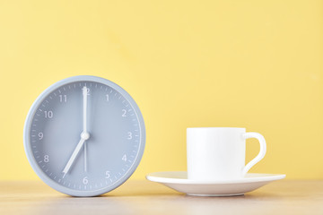 Fototapeta na wymiar Classic gray alarm clock and white coffee cup on a yellow background