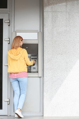Fototapeta na wymiar Beautiful woman using cash machine for money withdrawal outdoors. Space for text
