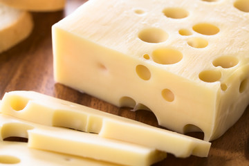 Piece of Emmental, Emmentaler or Emmenthal cheese on wooden plate (Selective Focus, Focus one third into the cheese piece) - obrazy, fototapety, plakaty