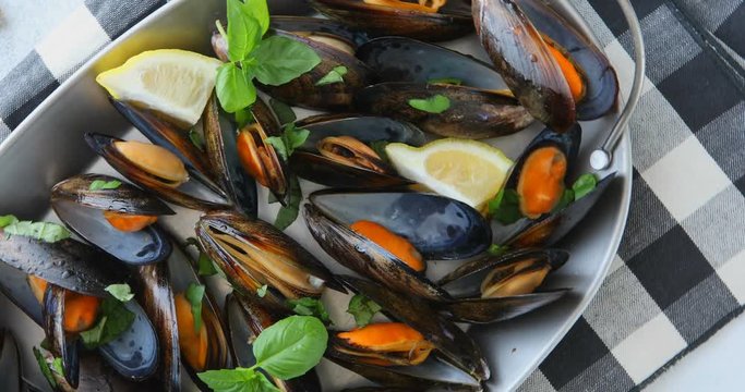 Shellfish mussels in copper bowl with lemon and herbs on white background with textile rotation 360. Shellfish seafood.