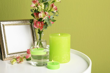Composition with burning candles, photo frame and fresh flowers on table near green wall. Space for text