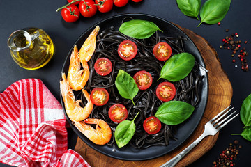 Black pasta (with black cuttlefish ink), cherry tomatoes, shrimps and basil on a black plate on a dark background